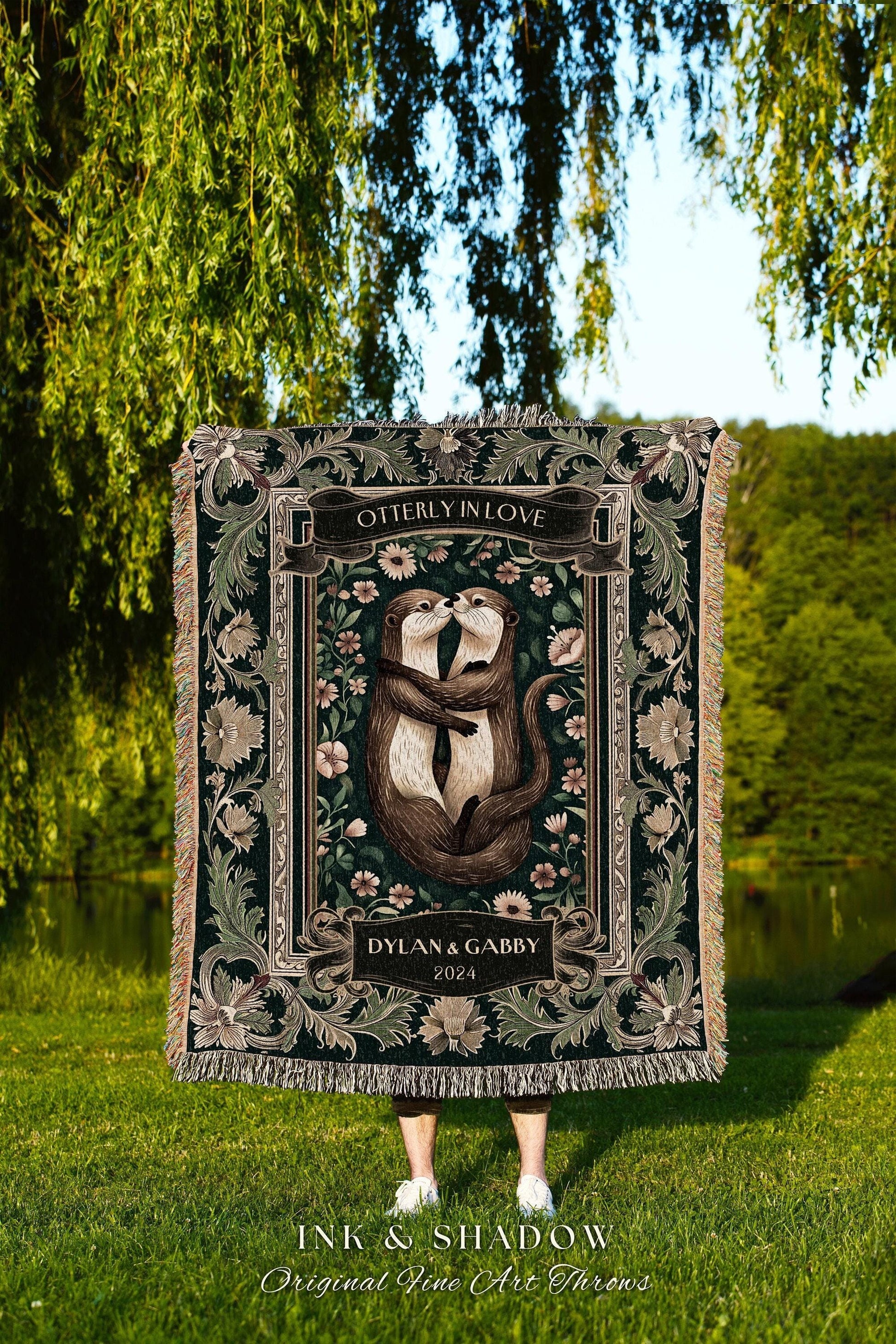 May include: A dark green throw blanket featuring a romantic illustration of two otters embracing, with the text "OTTERLY IN LOVE" and "DYLAN & GABBY 2024". The blanket has a decorative floral border and fringe.