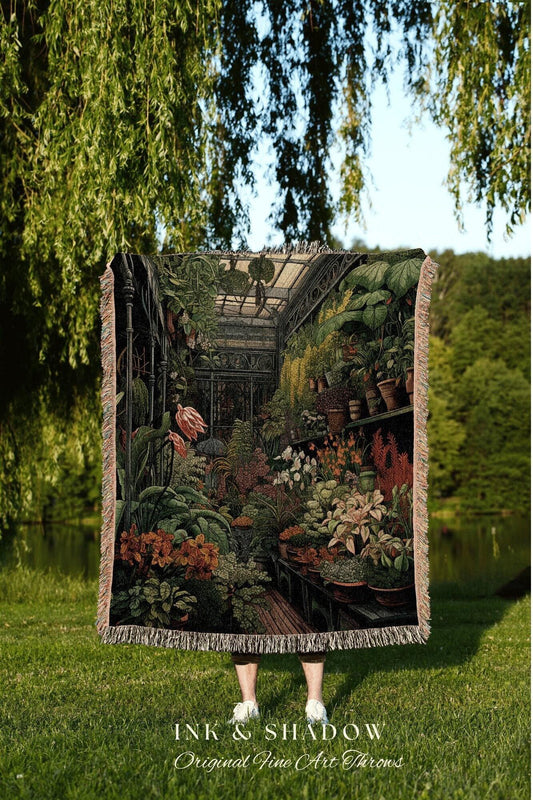 May include: A woven throw blanket featuring a detailed illustration of a greenhouse filled with various plants and flowers. The artwork showcases a variety of colors, including greens, browns, and reds, with a fringe border. The text "INK & SHADOW Original Fine Art Throws" is visible.