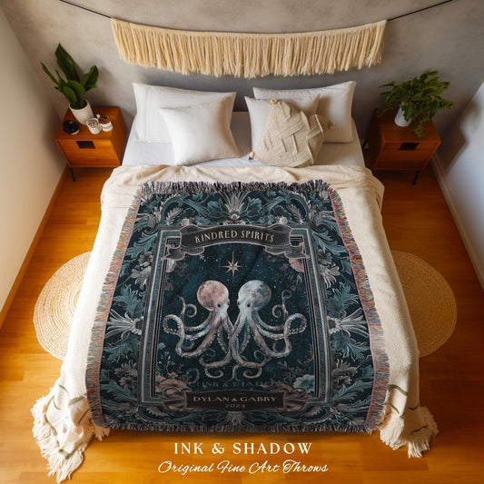 May include: A dark teal throw blanket with a decorative border and fringe. The center features two octopuses, one pink and one blue, with the text "KINDRED SPIRITS" and "INK & SHADOW Original Fine Art Throws". The blanket is on a bed with white pillows.