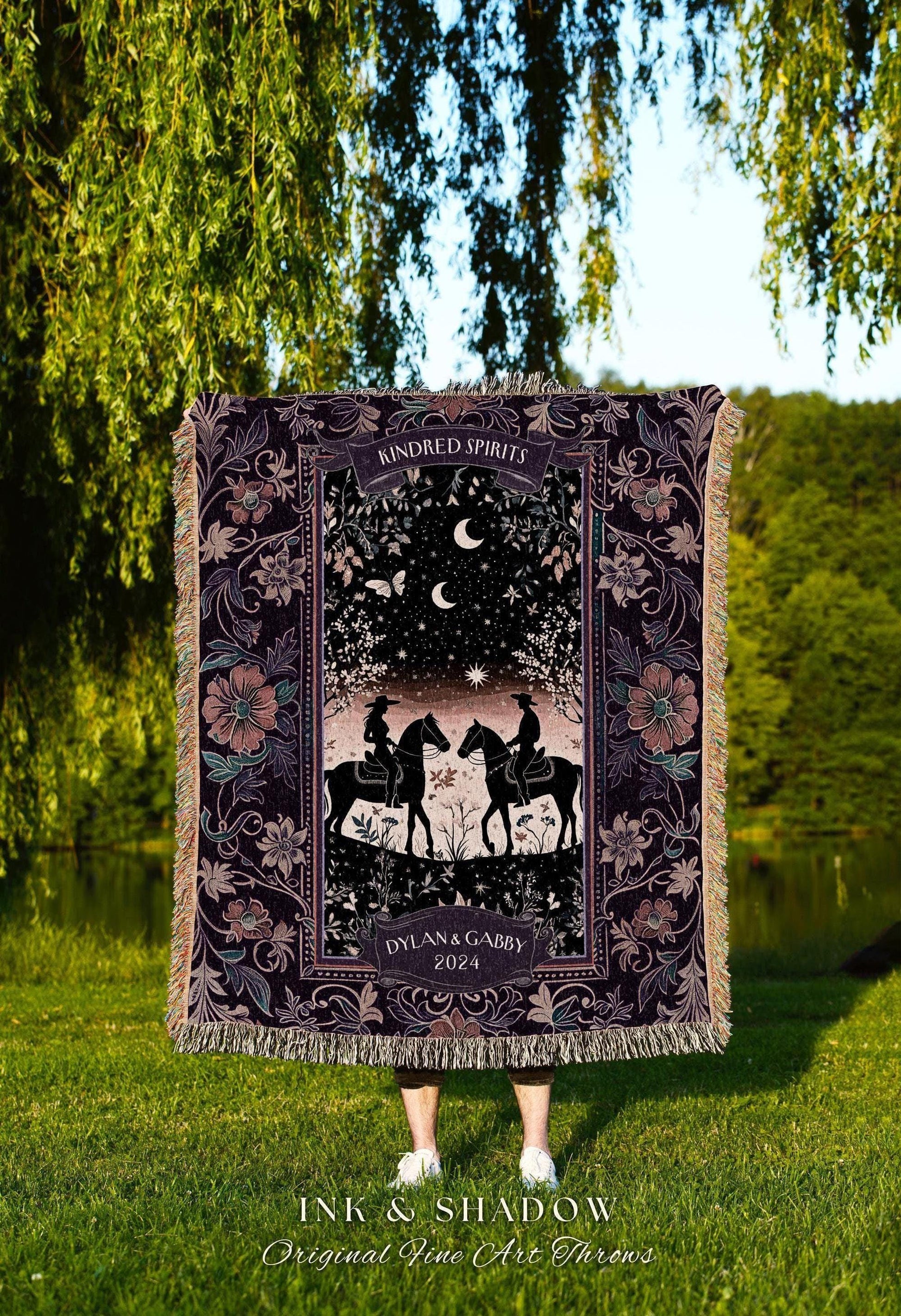 May include: A dark purple throw blanket with a romantic design featuring two riders on horseback under a starry night sky. The blanket has a floral border and the words "Kindred Spirits" and "Dylan & Gabby 2024".