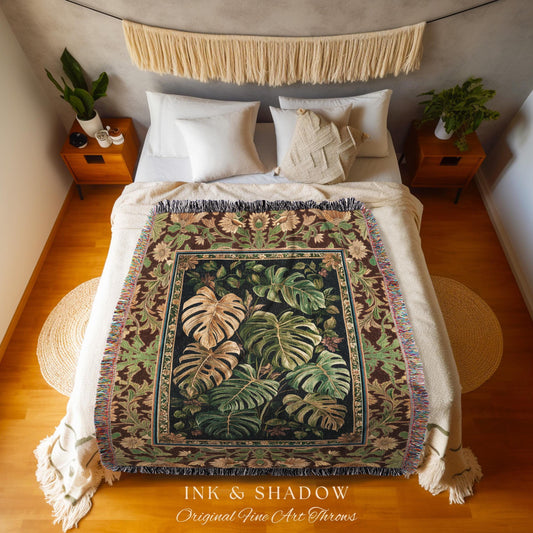May include: A woven throw blanket with a botanical design featuring large green and tan monstera leaves. The blanket has a dark brown border with floral and leaf patterns and a fringed edge. The text "INK & SHADOW Original Fine Art Throws" is at the bottom.