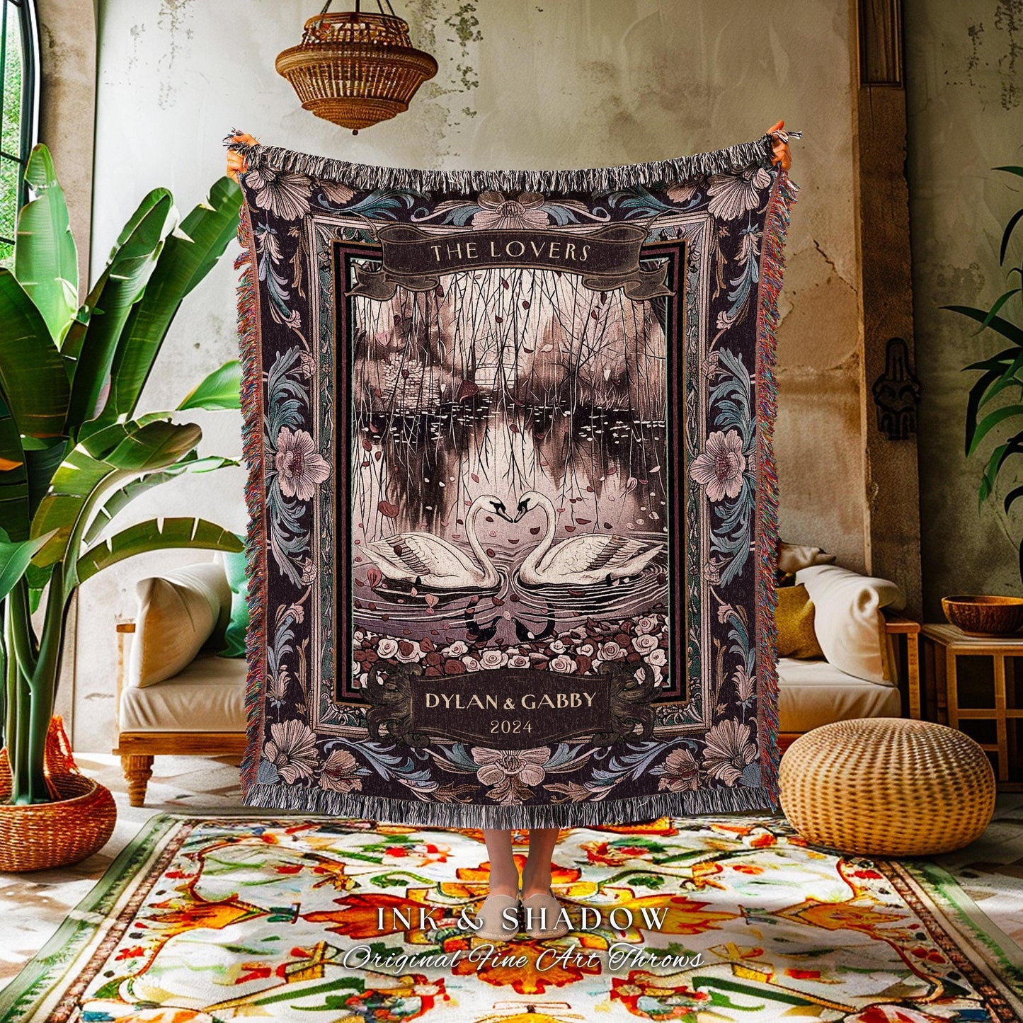 May include: A tapestry throw blanket featuring a romantic scene with two swans forming a heart shape on a lake. The blanket has a dark color palette with floral and foliage accents, and the text "THE LOVERS" is displayed at the top.