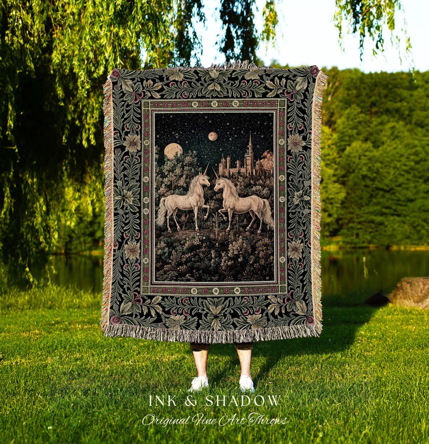 May include: A tapestry throw blanket featuring a fantasy scene with two unicorns, a castle, and celestial bodies. The blanket has a black border with floral and leaf patterns and fringe. The text "INK & SHADOW Original Fine Art Throws" is at the bottom.