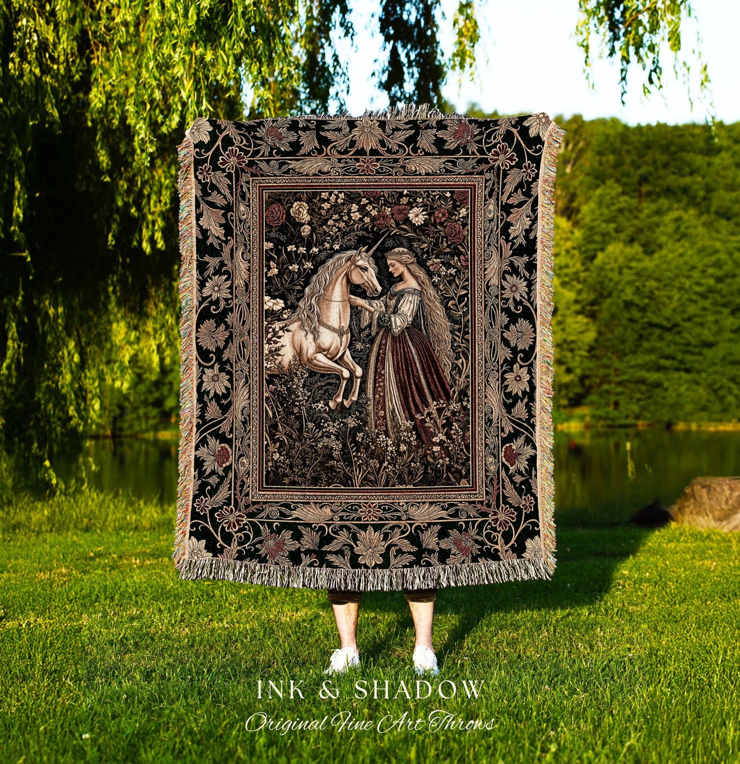 May include: A black woven tapestry throw blanket with a floral border and a central image of a woman in a long gown interacting with a white unicorn in a forest setting. The text 'INK & SHADOW Original Fine Art Throws' is printed below the blanket.