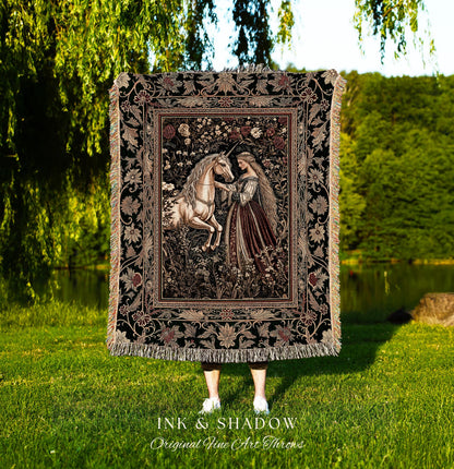 May include: A black woven tapestry throw blanket with a floral border and a central image of a woman in a long gown interacting with a white unicorn in a forest setting. The text 'INK & SHADOW Original Fine Art Throws' is printed below the blanket.