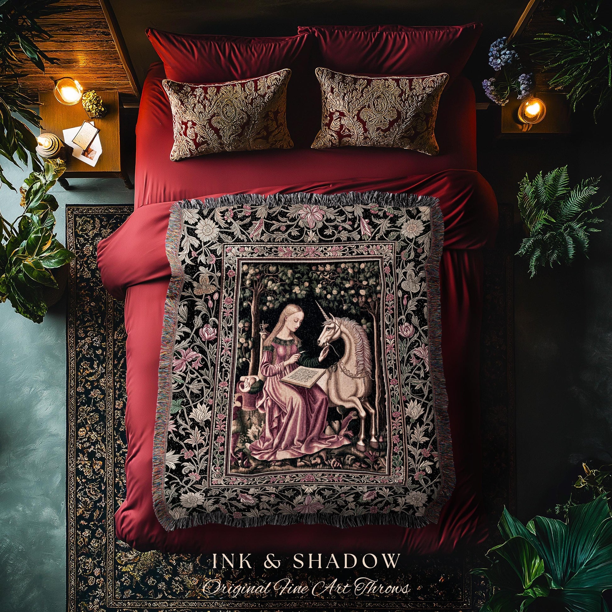 May include: A tapestry throw blanket featuring a woman and a unicorn in a forest scene. The throw has a black border with floral designs and fringe. The text "INK & SHADOW Original Fine Art Throws" is at the bottom. The blanket is on a red bed with matching pillows.