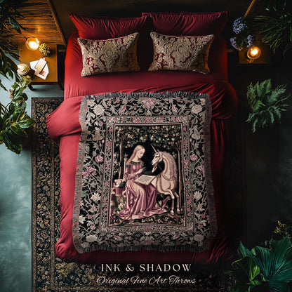 May include: A tapestry throw blanket featuring a woman and a unicorn in a forest scene. The throw has a black border with floral designs and fringe. The text "INK & SHADOW Original Fine Art Throws" is at the bottom. The blanket is on a red bed with matching pillows.