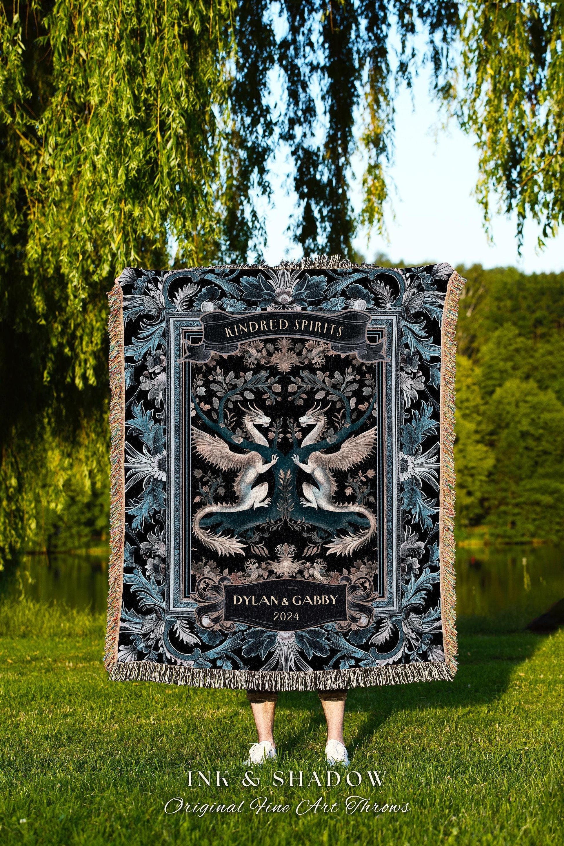 May include: A black and teal Kindred Spirits throw blanket featuring a symmetrical design of two dragons with outstretched wings. The blanket has a decorative border and the names Dylan & Gabby, and the year 2024 are displayed.