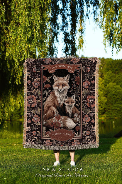 May include: A decorative throw blanket featuring a detailed illustration of two foxes, surrounded by floral patterns. The blanket has a black background with brown and pink accents, and the text "LOVE GROWS HERE" and "FOREVER & ALWAYS".