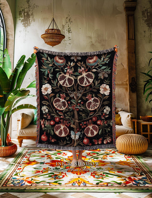 May include: Black throw blanket with a pomegranate tree design. The blanket features red, white, and blue accents, with a fringed edge. The blanket is held up in front of a colorful rug.