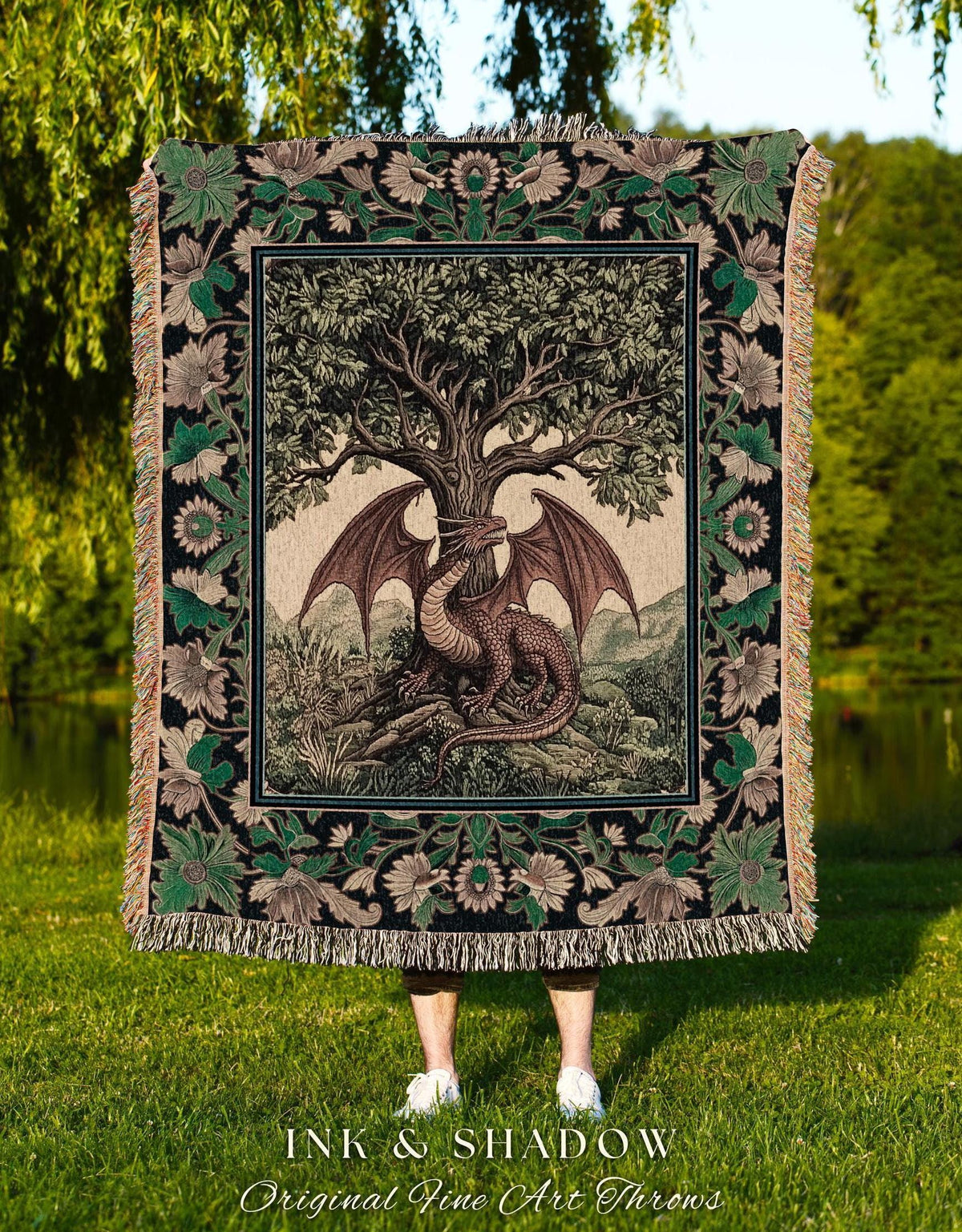 May include: A tapestry throw blanket featuring a detailed illustration of a dragon resting beneath a large tree. The dragon is brown with large wings. The blanket has a black border with floral and leaf patterns and fringe.