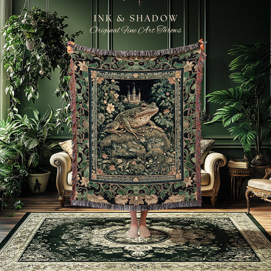 May include: A tapestry throw blanket featuring a large frog on a rock with a castle in the background. The throw has a dark green and black floral border and fringe. The text "INK & SHADOW Original Fine Art Throws" is at the top.
