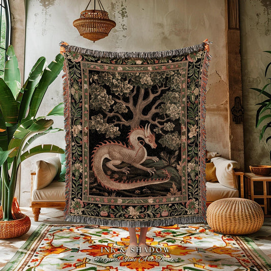 May include: A tapestry throw blanket featuring a dragon and tree design. The dragon is light brown with red accents, set against a black background with floral and tree details. The blanket has a fringed edge and the text "INK & SHADOW Original Fine Art Throws".