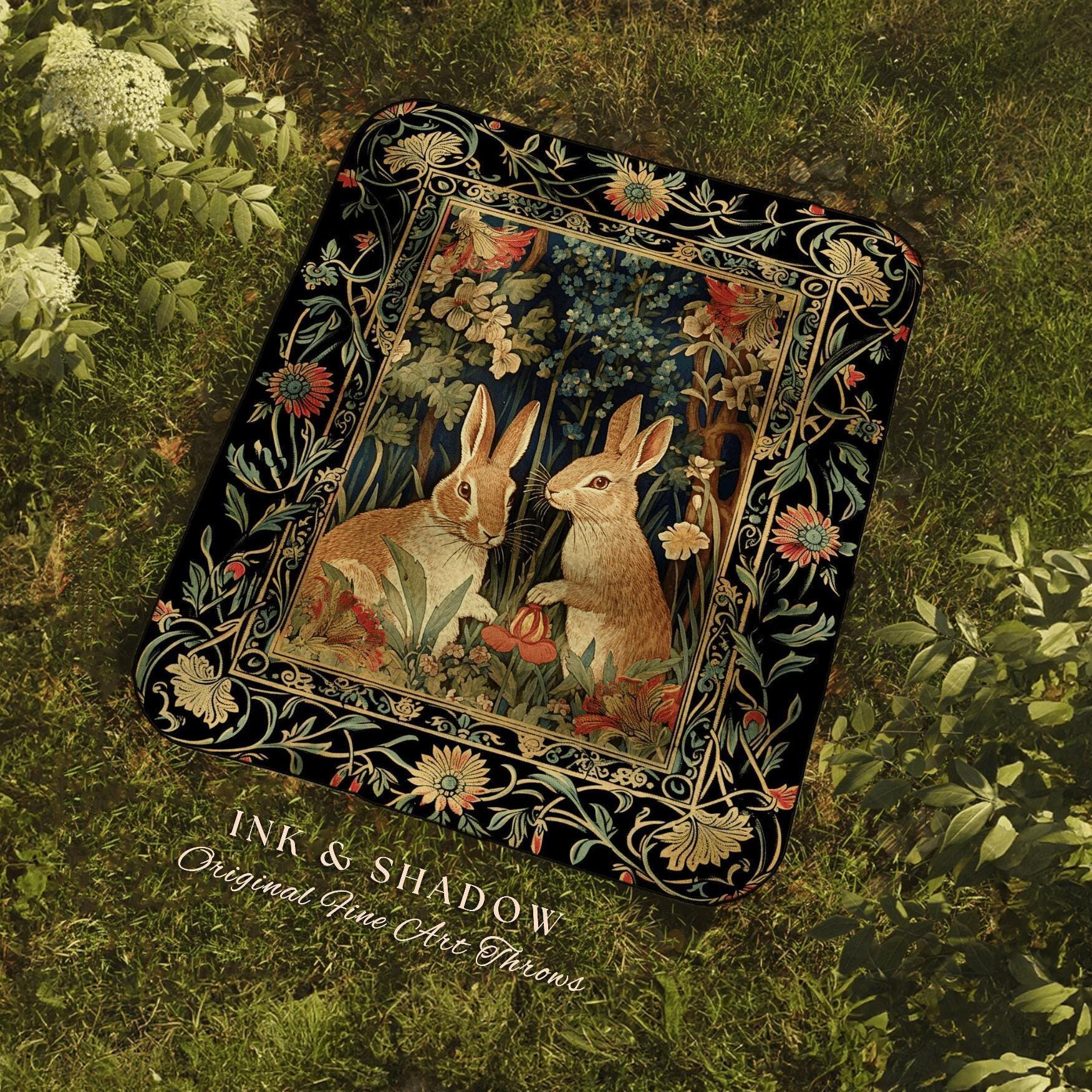 May include: A rectangular throw blanket featuring a detailed illustration of two rabbits in a forest setting. The artwork is framed by a black border with floral and vine motifs. The blanket has the text "INK & SHADOW Original Fine Art Throws".