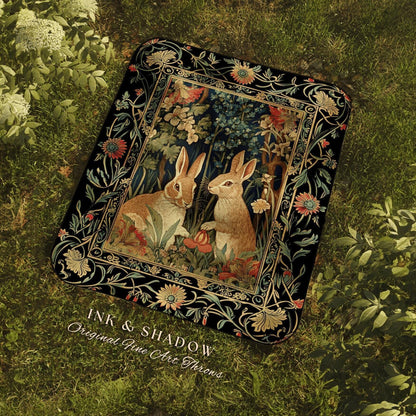May include: A rectangular throw blanket featuring a detailed illustration of two rabbits in a forest setting. The artwork is framed by a black border with floral and vine motifs. The blanket has the text "INK & SHADOW Original Fine Art Throws".
