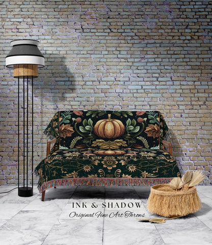 May include: A decorative throw blanket with a pumpkin design, draped over a wooden sofa. The blanket features a dark green background with a large pumpkin in the center, surrounded by leaves and floral patterns. The image also includes a floor lamp and a woven basket.