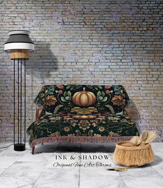 May include: A decorative throw blanket with a pumpkin design, draped over a wooden sofa. The blanket features a dark green background with a large pumpkin in the center, surrounded by leaves and floral patterns. The image also includes a floor lamp and a woven basket.