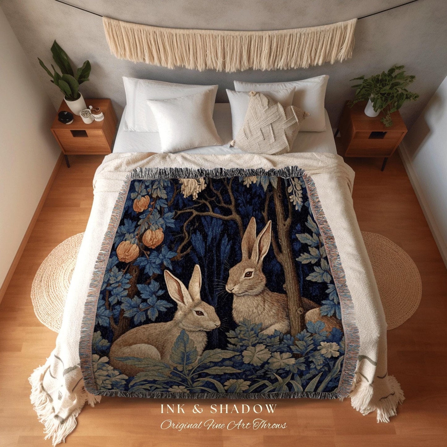 May include: A woven throw blanket featuring a forest scene with two rabbits, blue foliage, and orange fruit. The blanket has a dark blue background and a fringed edge. The text "INK & SHADOW Original Fine Art Throws" is at the bottom.