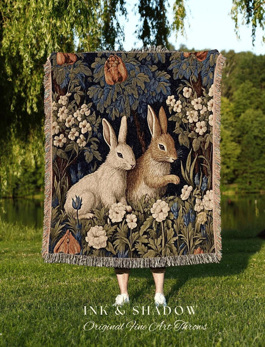May include: A tapestry throw blanket featuring two rabbits amidst a floral and foliage design in shades of blue, green, and beige. The blanket has a fringed edge and the text "INK & SHADOW Original Fine Art Throws" at the bottom.