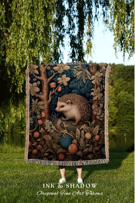 May include: A tapestry throw blanket featuring a detailed illustration of a hedgehog in a forest scene with trees, berries, and foliage. The blanket has a fringed edge and the text "INK & SHADOW Original Fine Art Throws".