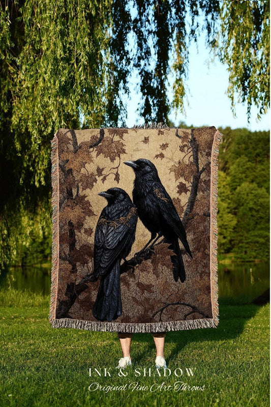 May include: A woven throw blanket featuring two black crows perched on a branch, set against a brown and tan background with a leaf pattern. The blanket has a fringed edge and the text "INK & SHADOW Original Fine Art Throws".