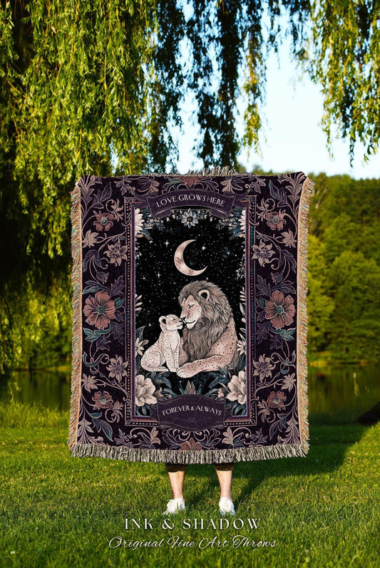 May include: A woven throw blanket with a lion and cub illustration under a crescent moon and stars. The blanket has a dark background with floral accents and the text "LOVE GROWS HERE" and "FOREVER & ALWAYS". The blanket has a fringed edge.