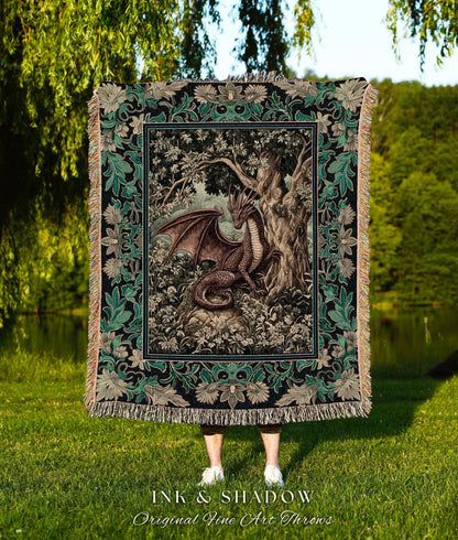 May include: A decorative throw blanket featuring a detailed illustration of a dragon in a forest setting. The blanket has a black border with green floral accents and a fringed edge. The text "INK & SHADOW Original Fine Art Throws" is at the bottom.