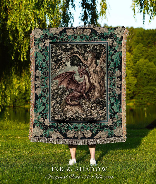 May include: A decorative throw blanket featuring a detailed illustration of a dragon in a forest setting. The blanket has a black border with green floral accents and a fringed edge. The text "INK & SHADOW Original Fine Art Throws" is at the bottom.