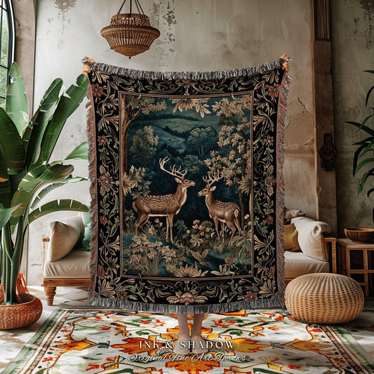 May include: A tapestry throw blanket featuring a forest scene with two deer. The blanket has a dark background with a detailed floral border and fringe. The text "INK & SHADOW Original Fine Art Throws" is at the bottom.