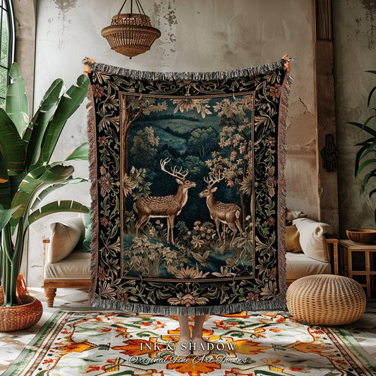 May include: A tapestry throw blanket featuring a forest scene with two deer. The blanket has a dark background with a detailed floral border and fringe. The text "INK & SHADOW Original Fine Art Throws" is at the bottom.
