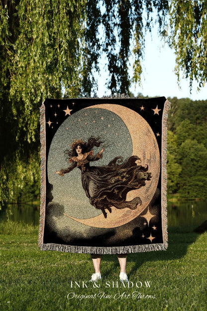 May include: A black throw blanket featuring a celestial design with a woman riding a crescent moon, surrounded by stars. The blanket has a fringed edge and the text "INK & SHADOW Original Fine Art Throws" at the bottom. The color palette includes black, gold, and gray.