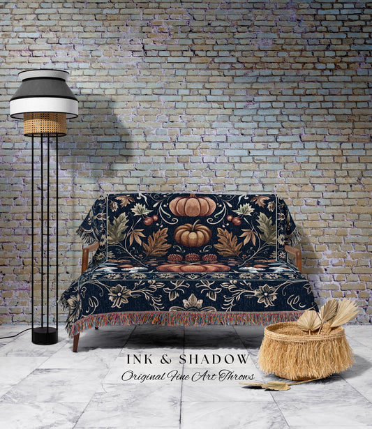 May include: A navy blue throw blanket with a pumpkin and floral design, draped over a wooden sofa. The blanket has a fringed edge. The image also shows a floor lamp and a woven basket.