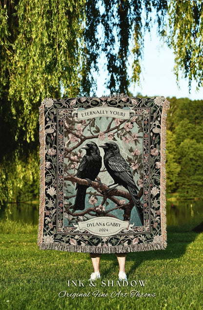 May include: A decorative throw blanket featuring two black crows perched on a flowering branch. The blanket has a black and floral border with the text "Eternally Yours" and "Dylan & Gabby 2024". The blanket is displayed outdoors on a sunny day.