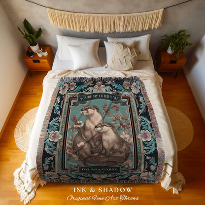 May include: A decorative throw blanket featuring two otters with the text "YOU'RE MY OTTER HALF" and the names "DYLAN & GABBY 2024". The blanket has a teal background with floral and botanical accents. The bottom of the blanket reads "INK & SHADOW Original Fine Art Throws".
