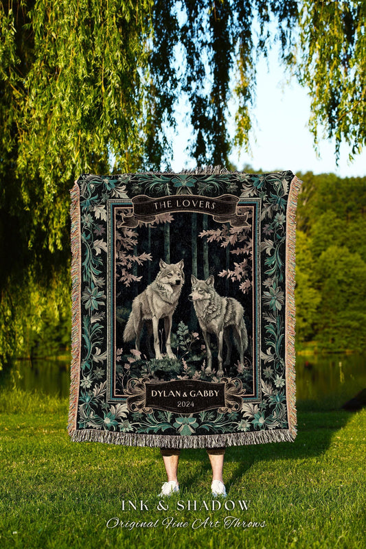 May include: A woven throw blanket featuring a forest scene with two wolves. The blanket has a black background with floral and leaf accents. Text includes "THE LOVERS", "DYLAN & GABBY 2024", and "INK & SHADOW Original Fine Art Throws".