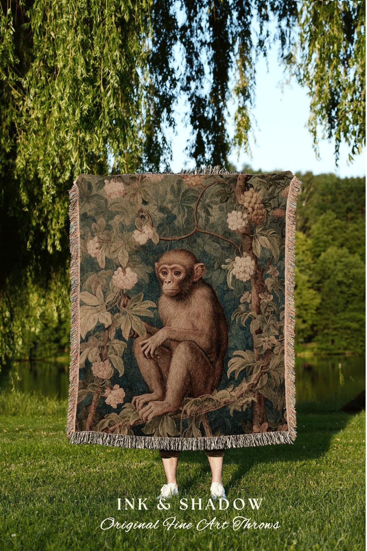 May include: A tapestry throw blanket featuring a detailed illustration of a monkey sitting in a tree, surrounded by foliage and flowers. The blanket has a fringed edge and the text "INK & SHADOW Original Fine Art Throws" at the bottom.