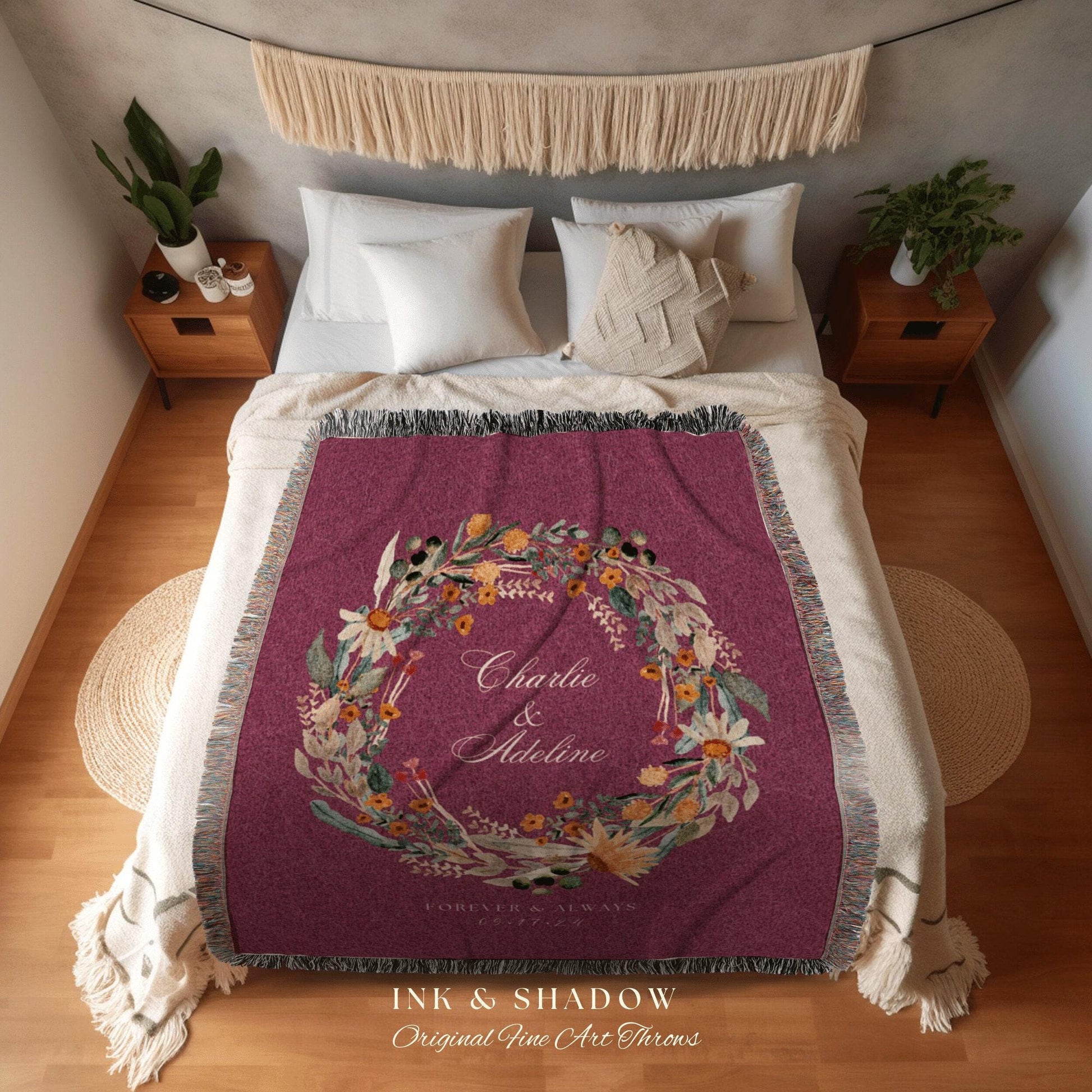 May include: A burgundy throw blanket with a floral wreath design, featuring the names "Charlie & Adeline" and the text "Forever & Always." The blanket has a fringed edge and is displayed on a bed with white pillows and a macrame wall hanging.