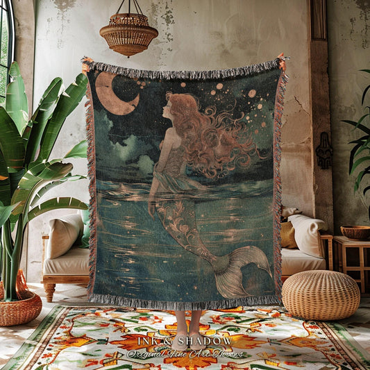 May include: A woven throw blanket featuring a mermaid illustration. The artwork depicts a mermaid with flowing red hair, a crescent moon, and a starry night sky. The blanket has a fringed edge and the text "INK & SHADOW Original Fine Art Throws".