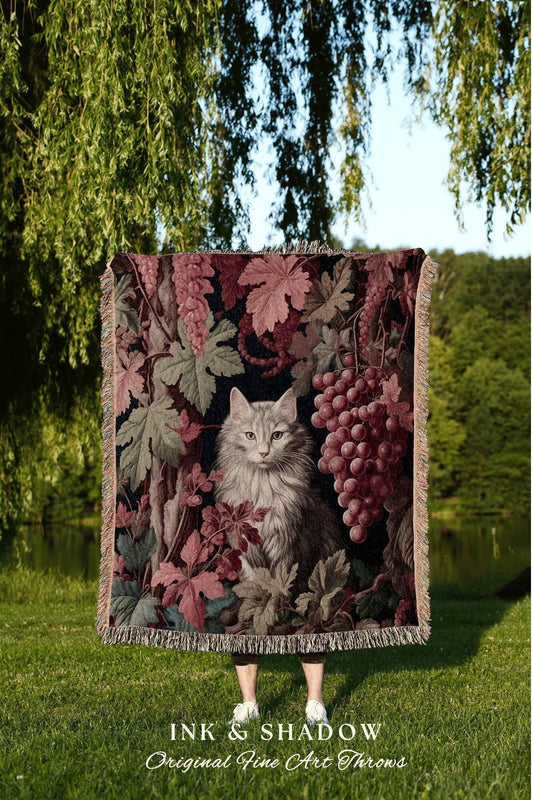 May include: A woven throw blanket featuring a detailed illustration of a gray cat amidst grape vines and leaves in shades of burgundy, green, and brown. The blanket has a fringed edge and the text "INK & SHADOW Original Fine Art Throws" at the bottom.