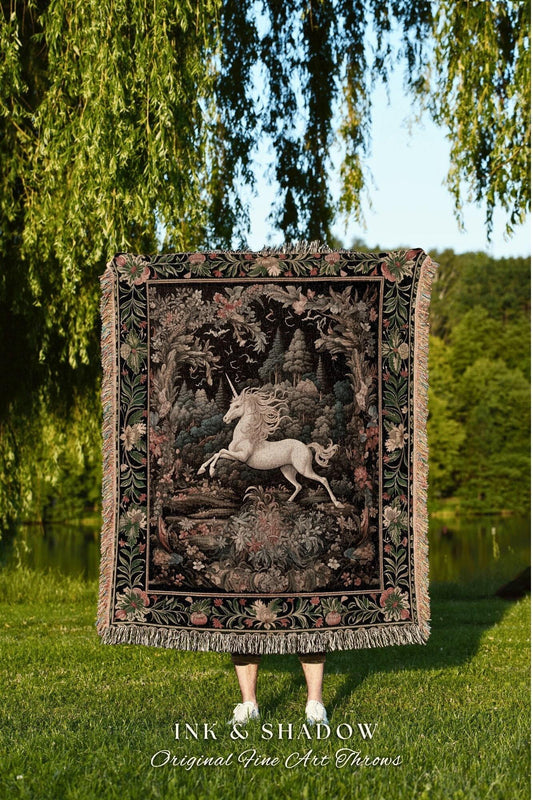 May include: A tapestry throw blanket featuring a white unicorn in a forest scene. The throw has a black background with floral and foliage details, and a fringed edge. The text "INK & SHADOW Original Fine Art Throws" is at the bottom.