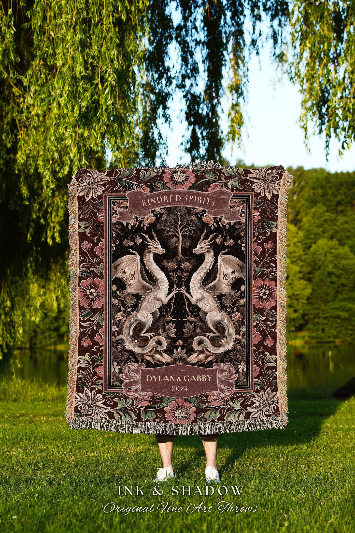 May include: A decorative throw blanket featuring a symmetrical design of two dragons facing each other, with the words "Kindred Spirits" and "Dylan & Gabby 2024". The blanket has a floral border and fringe.