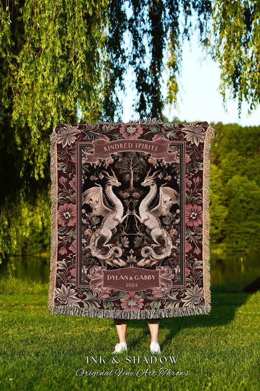May include: A decorative throw blanket featuring a symmetrical design of two dragons facing each other, with the words "Kindred Spirits" and "Dylan & Gabby 2024". The blanket has a floral border and fringe.