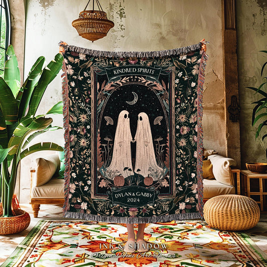 May include: A dark green woven throw blanket with a central design featuring two ghost figures holding hands under a crescent moon. The blanket has a floral border and the text "Kindred Spirits" and "Dylan & Gabby 2024".