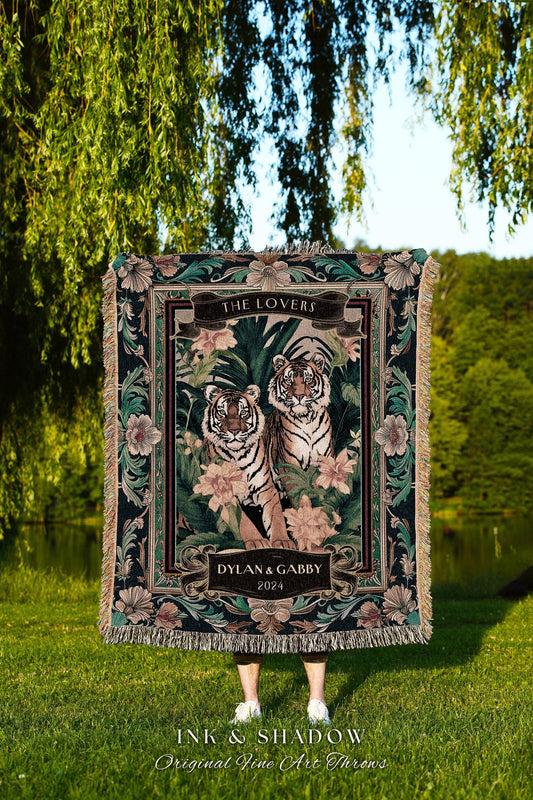 May include: A decorative throw blanket featuring two tigers amidst floral and foliage elements. The design includes the text "THE LOVERS" and "DYLAN & GABBY 2024". The blanket has a dark green border with fringe.