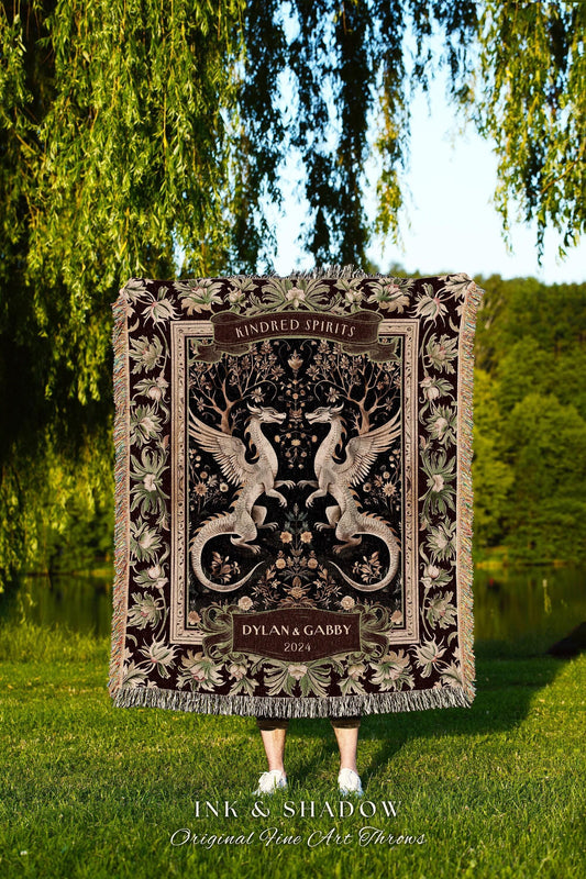 May include: A burgundy throw blanket with a detailed design featuring two winged dragons facing each other. The blanket has a floral border and the words "Kindred Spirits" and "Dylan & Gabby 2024". The blanket is fringed and has the text "INK & SHADOW Original Fine Art Throws".