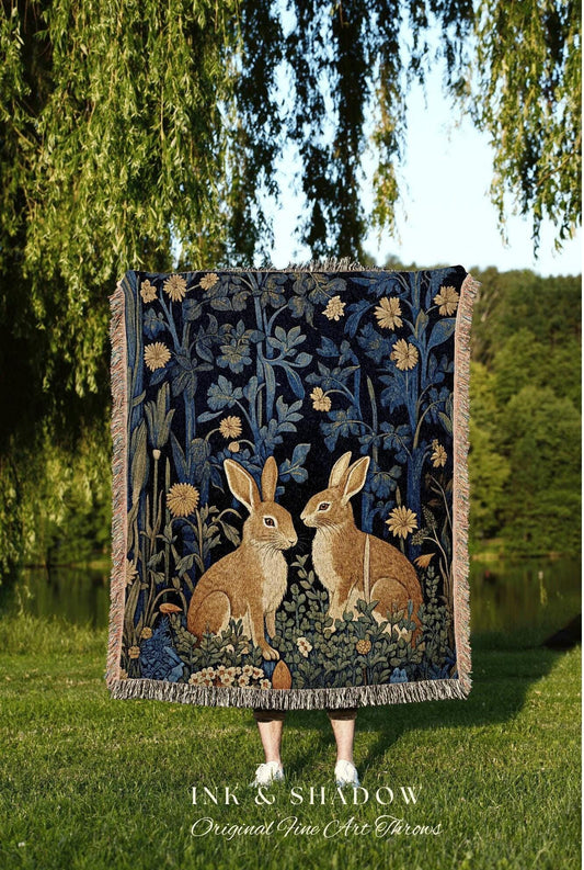 May include: A dark blue throw blanket with a forest scene featuring two brown rabbits. The blanket has a floral design with yellow and blue accents and a fringed edge. The text "INK & SHADOW Original Fine Art Throws" is at the bottom.