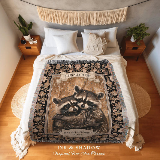 May include: A woven throw blanket featuring a sepia-toned illustration of two raccoons embracing. The blanket has a black border with floral patterns and the text "Eternally Yours" and "Dylan & Gabby 2024". The words "INK & SHADOW Original Fine Art Throws" are at the bottom.