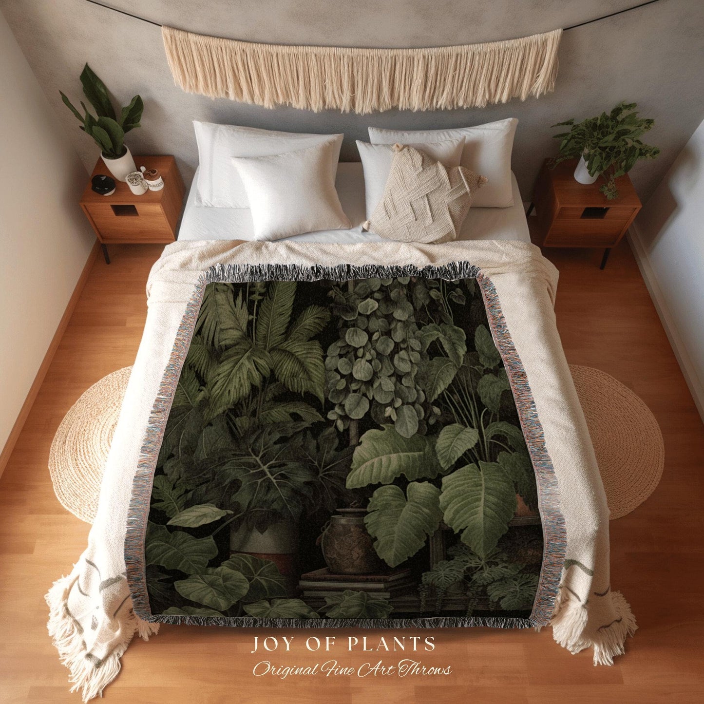 May include: A woven throw blanket featuring a botanical print of lush green plants and foliage. The blanket is draped over a bed with white bedding. The text "JOY OF PLANTS" and "Original Fine Art Throws" is visible.
