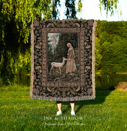 May include: A decorative throw blanket featuring a detailed forest scene with a woman and a deer. The blanket has a black background with floral and leaf border designs and fringe. The text "INK & SHADOW Original Fine Art Throws" is at the bottom.
