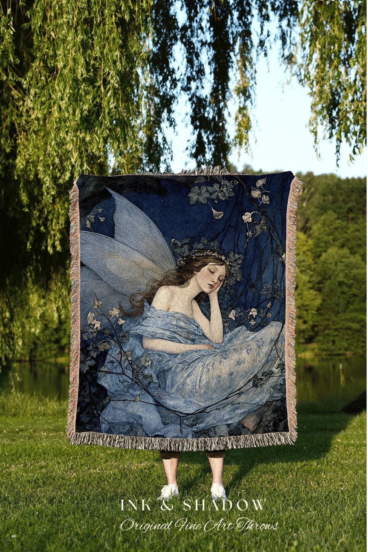 May include: A woven throw blanket featuring a fairy illustration in shades of blue, with a fringe border. The artwork depicts a sleeping fairy with large wings, surrounded by foliage. The blanket has the text "INK & SHADOW Original Fine Art Throws".